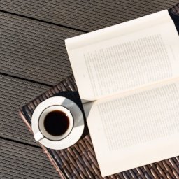 FHU Heda Adam Heda - Kompozycja z filiżanką czarnej kawy i otwartą książką na drewnianym tarasie kompozytowym w słoneczny dzień.