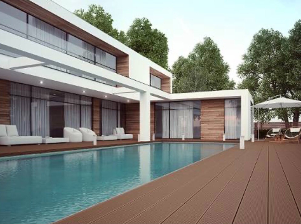 Nowoczesny dom z basenem i drewnianym tarasem, białe meble ogrodowe i parasol, duże okna z zasłonami, otoczony zielenią.