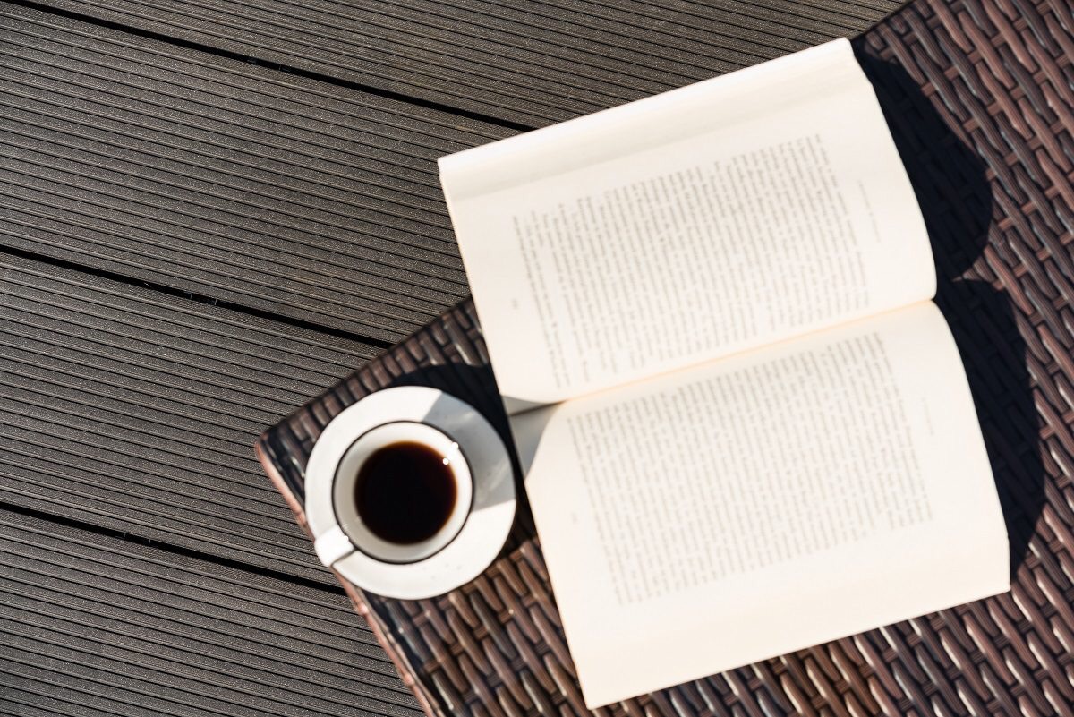 Kompozycja z filiżanką czarnej kawy i otwartą książką na drewnianym tarasie kompozytowym w słoneczny dzień.