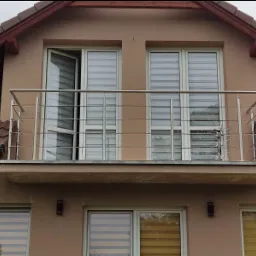 Balkon z prostą, nowoczesną metalową balustradą, widok z dołu na elewację domu z oknami i roletami.