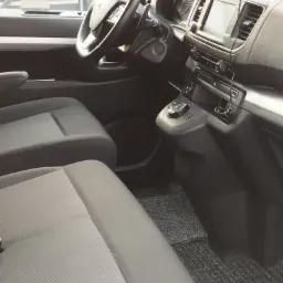 Wnętrze busa z szarymi fotelami, widoczna deska rozdzielcza z ekranem nawigacji i panel sterowania, dywaniki podłogowe w kolorze grafitowym.