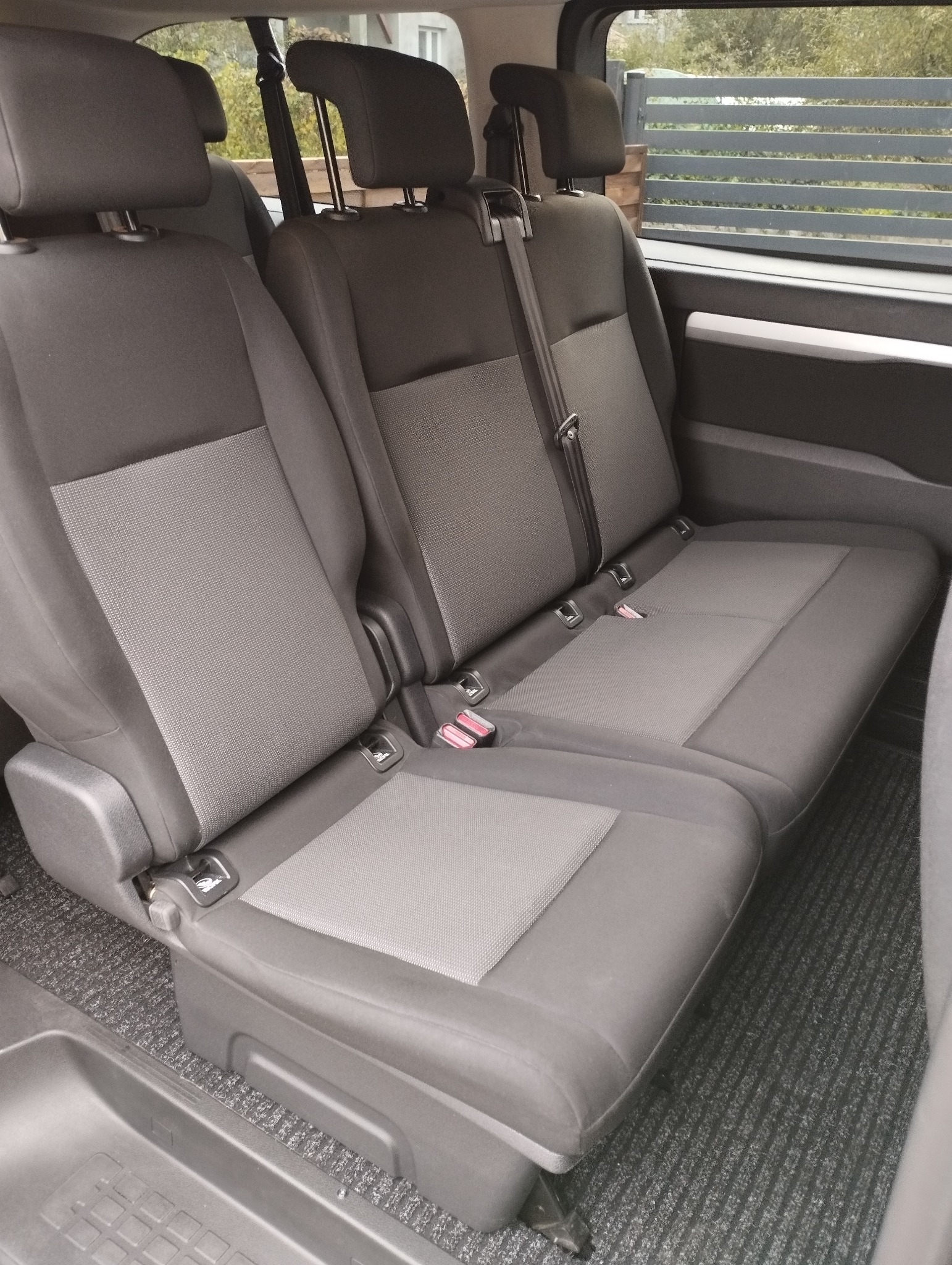 Wnętrze samochodu z dwoma rzędami szarych, tekstylnych siedzeń pasażerskich z pasami bezpieczeństwa, widok z perspektywy bagażnika.