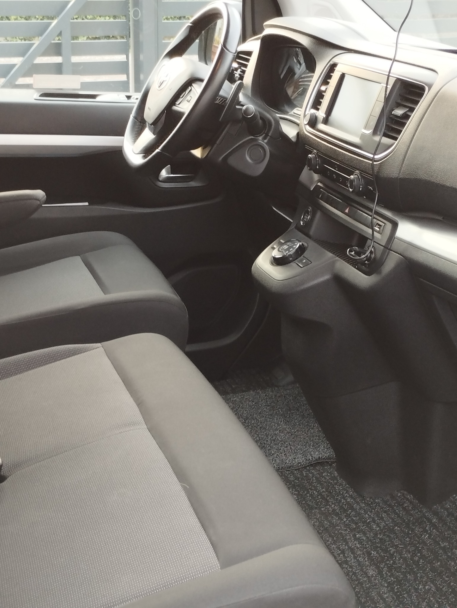 Wnętrze busa z szarymi fotelami, widoczna deska rozdzielcza z ekranem nawigacji i panel sterowania, dywaniki podłogowe w kolorze grafitowym.