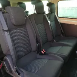 Wnętrze busa z trzema rzędami siedzeń w kolorze ciemnoszarym z pasami bezpieczeństwa, widok z boku.