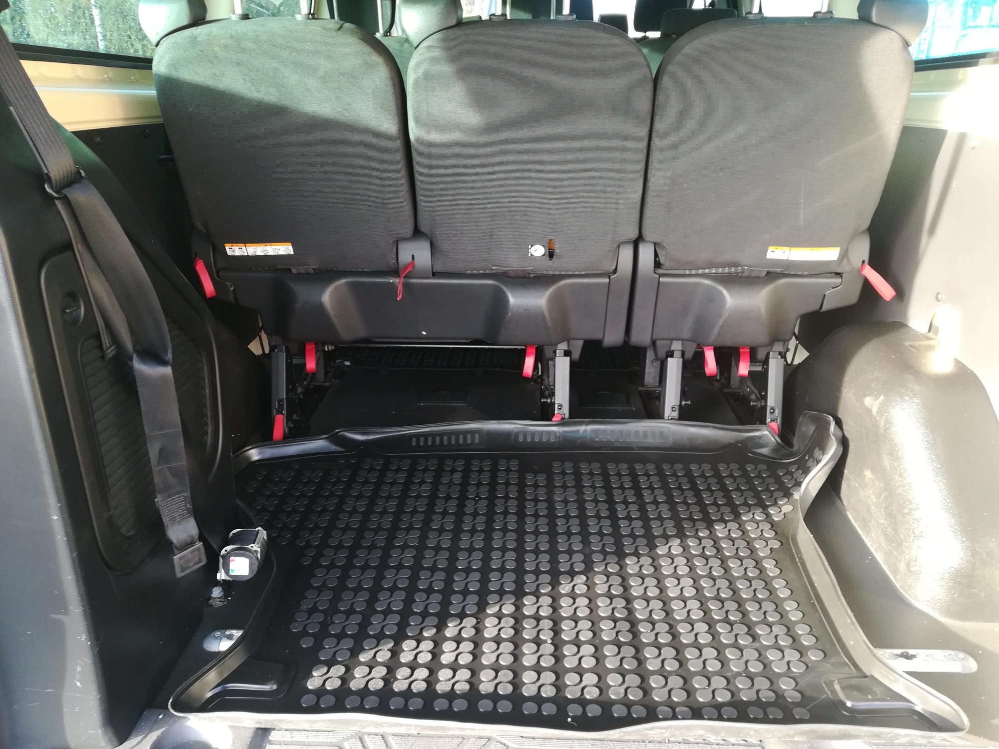 Wnętrze bagażnika busa z trzema rzędami składanych foteli i gumową wycieraczką z okrągłymi wypustkami.
