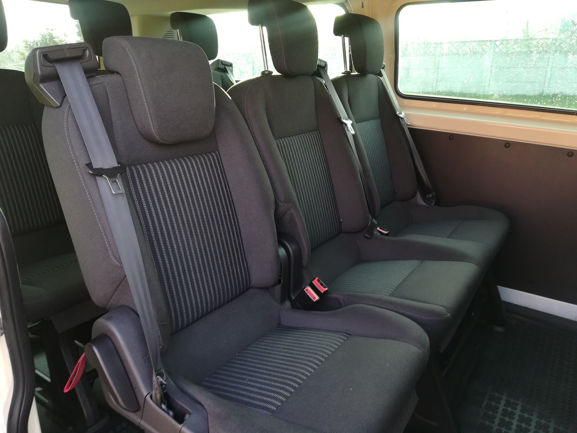 Wnętrze busa z trzema rzędami siedzeń w kolorze ciemnoszarym z pasami bezpieczeństwa, widok z boku.