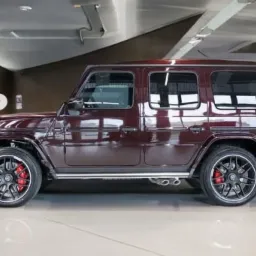 Burgundowy samochód terenowy z czarnymi felgami i czerwonymi zaciskami hamulcowymi, widok z boku w salonie samochodowym.