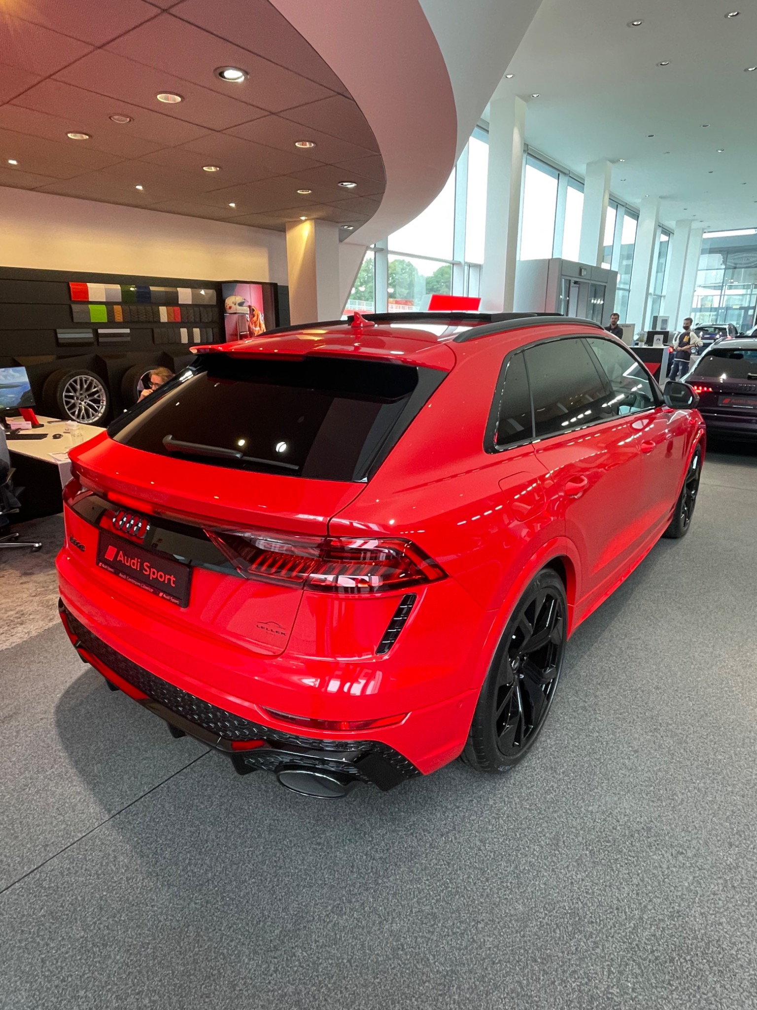 Czerwony samochód Audi Sport z czarnymi felgami prezentowany w salonie, widok z tyłu, z widocznym logo Audi Sport.