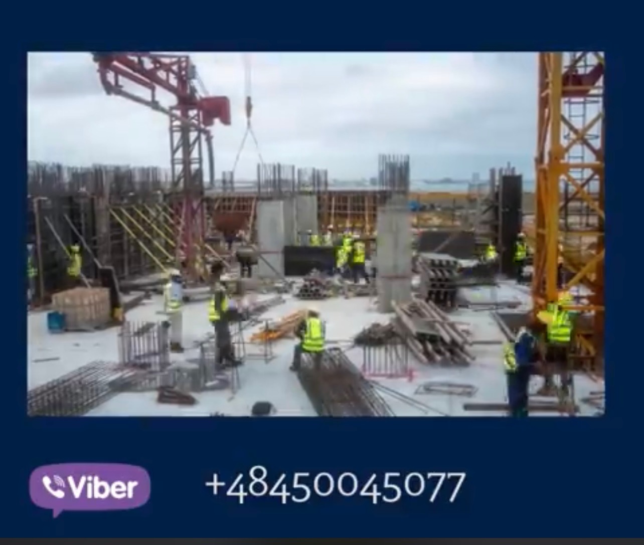 Widok z góry na plac budowy z pracownikami w kamizelkach odblaskowych, dźwigami i zbrojeniami, w tle widoczne morze.