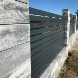 Nowoczesne ogrodzenie posesji z szarej, poziomej sztachet oraz betonowych słupków i podmurówki, z metalową skrzynką na listy.