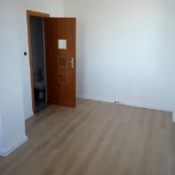 Jasne panele podłogowe w pokoju w Nowej Woli, widok na otwarte drzwi do łazienki z białymi ścianami i listwami przypodłogowymi.