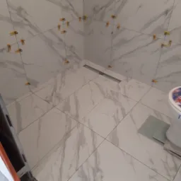 Montaż płytek imitujących marmur w łazience z widocznym odpływem liniowym i klipsami poziomującymi.