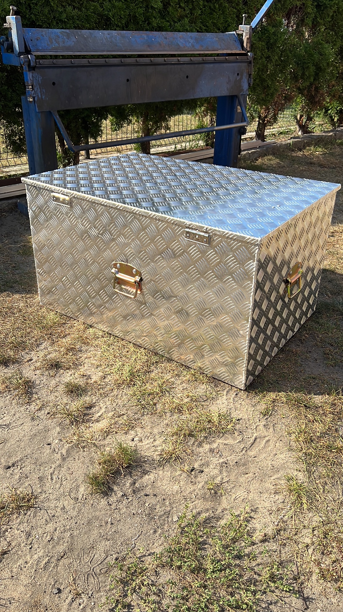 Aluminiowa skrzynia narzędziowa z uchwytami, wzór diamentowy, na zewnątrz w Kadłubiu. W tle giętarka do blachy.