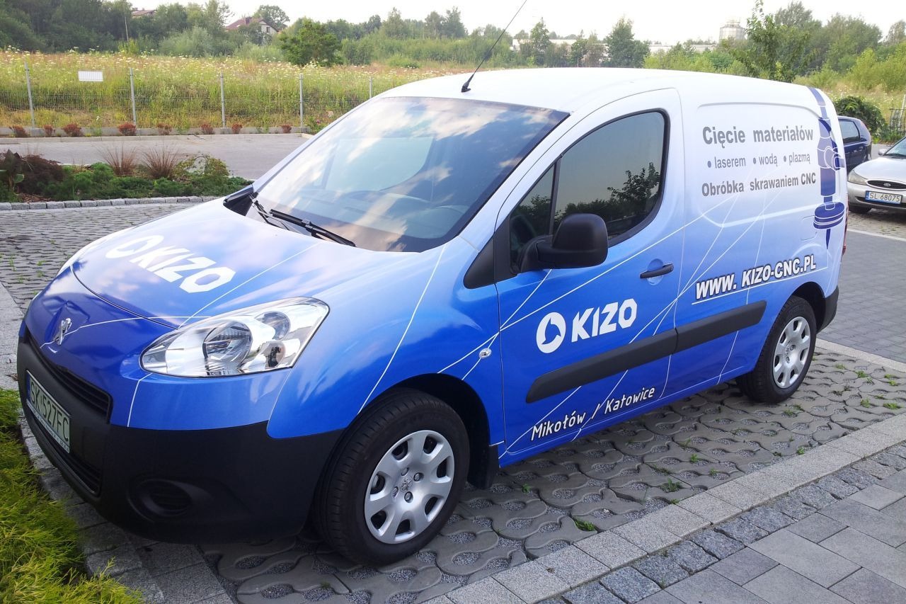 Niebiesko-biały samochód dostawczy z logo KIZO i informacją o cięciu materiałów laserem, wodą, plazmą oraz obróbce skrawaniem CNC, zaparkowany na kostce brukowej.