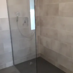 Nowoczesna kabina prysznicowa typu walk-in z szarymi płytkami imitującymi kamień na ścianach i podłodze, deszczownica zamontowana na suficie.