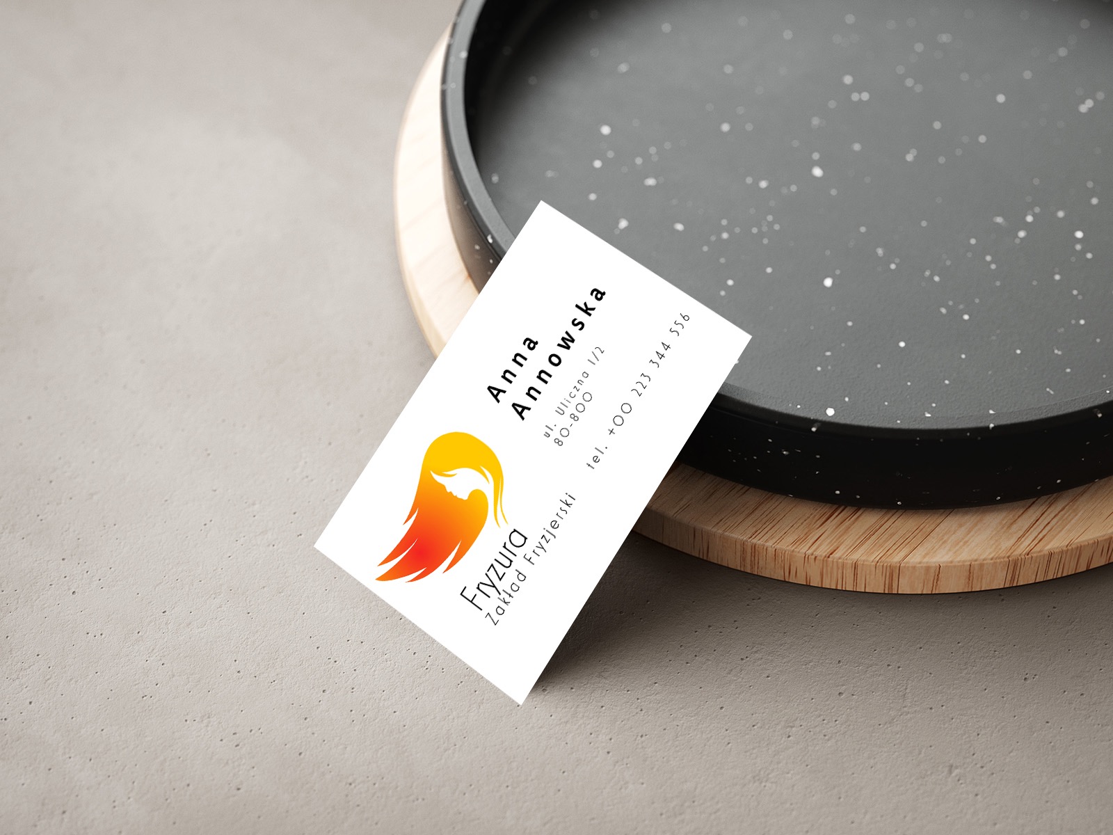 Wizytówka salonu fryzjerskiego z logo przedstawiającym profil kobiety z płomiennymi włosami w odcieniach żółci i czerwieni, leżąca na dekoracyjnej tacy.