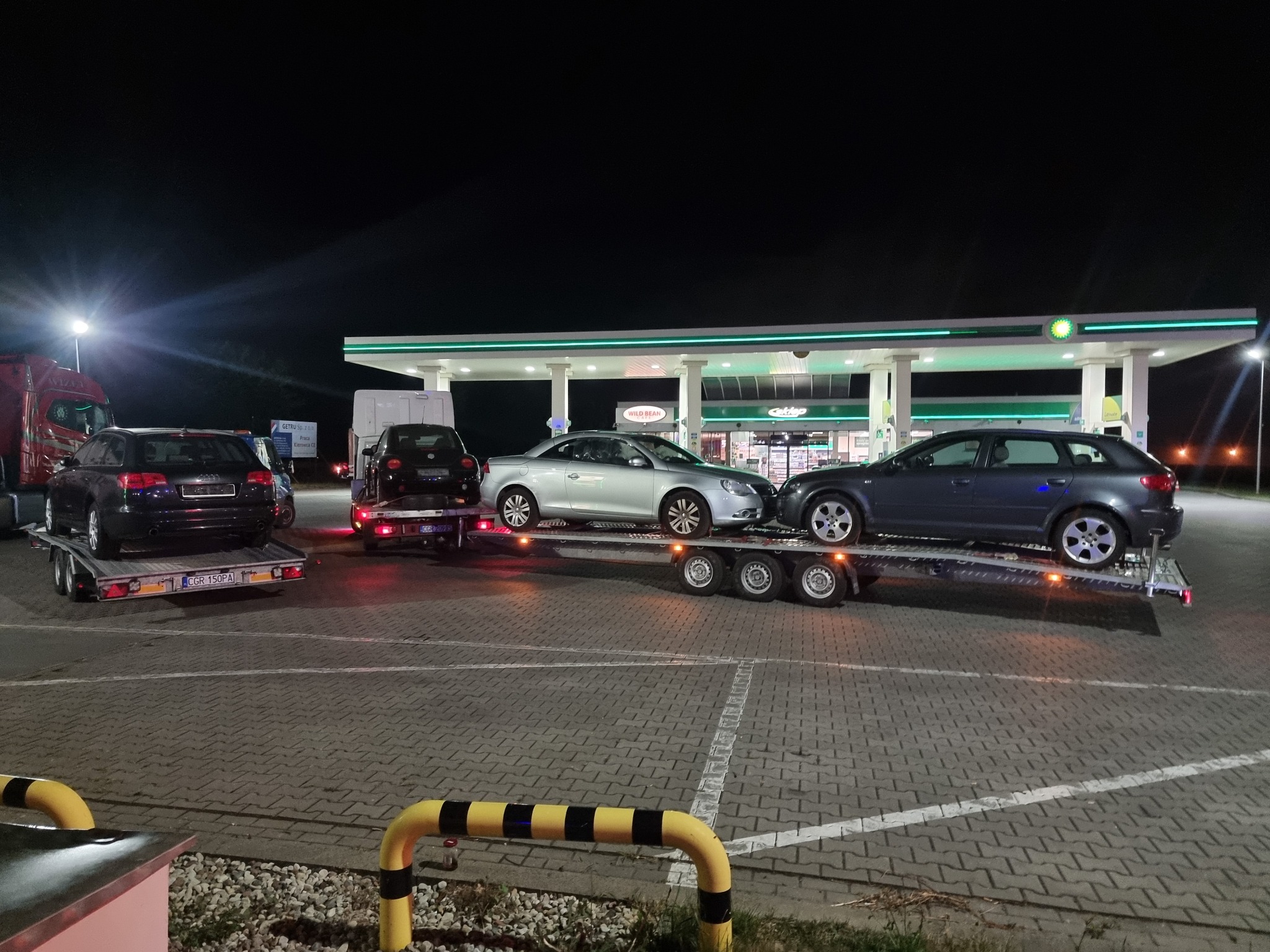 Nocny transport trzech samochodów na lawetach w Grudziądzu, na tle stacji benzynowej BP, widoczne numery rejestracyjne pojazdów.