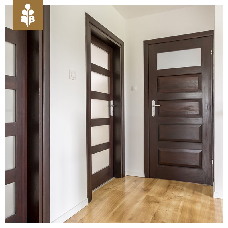 Korytarz z trzema ciemnobrązowymi drzwiami z przeszkleniami, widoczne ościeżnice i klamki, podłoga laminowana w kolorze jasnego drewna.