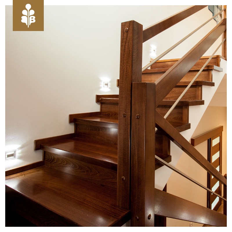 Polerowane, ciemne schody drewniane z metalową balustradą, oświetlone subtelnymi kinkietami ściennymi.