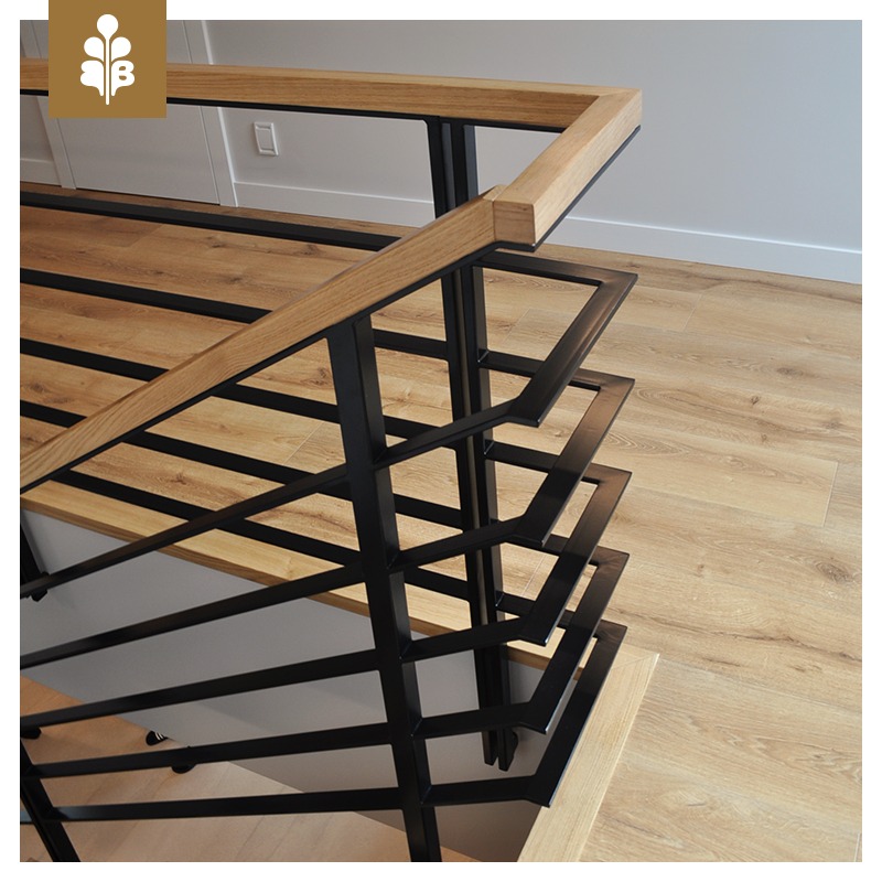 Nowoczesne schody o drewnianych stopniach i czarnej, metalowej balustradzie z geometrycznym wzorem, widok z góry.