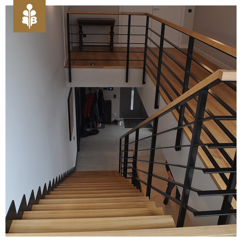 Drewniane schody z czarną balustradą w domu w Krakowie, widok z góry, oświetlenie dzienne, minimalistyczny design.