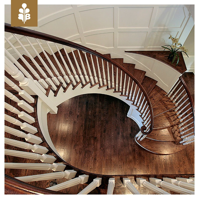 Eleganckie, kręte schody drewniane z białymi balustradami, widok z góry na ciemne, lakierowane stopnie i parkiet, z dekoracyjnym sufitem kasetonowym w tle.