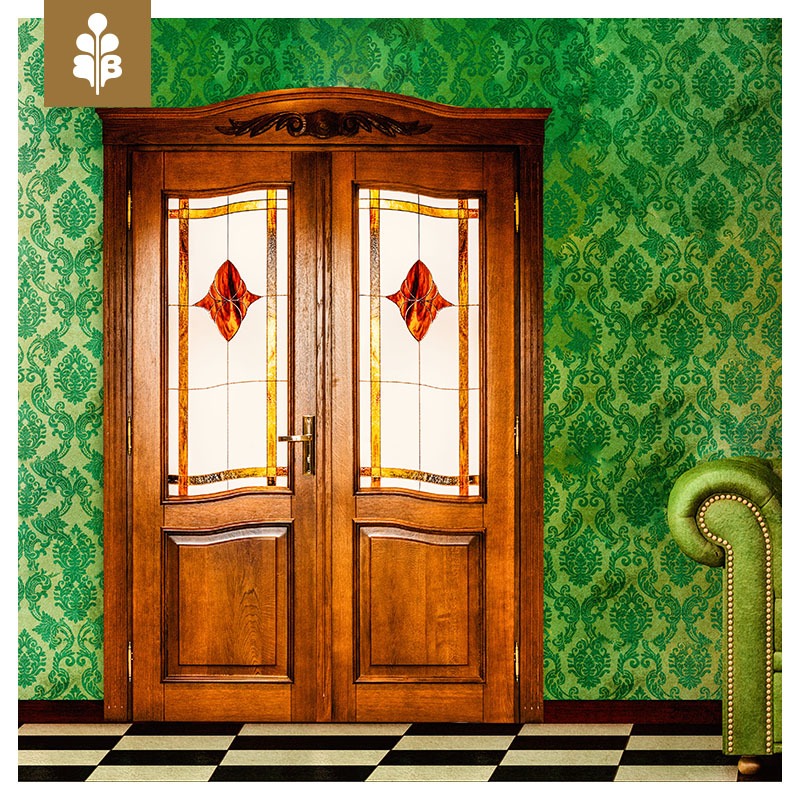 Dwuskrzydłowe, fornirowane drzwi z szybami witrażowymi w odcieniach czerwieni i złota, na tle zielonej ściany w ornamenty i czarno-białej podłogi w szachownicę.