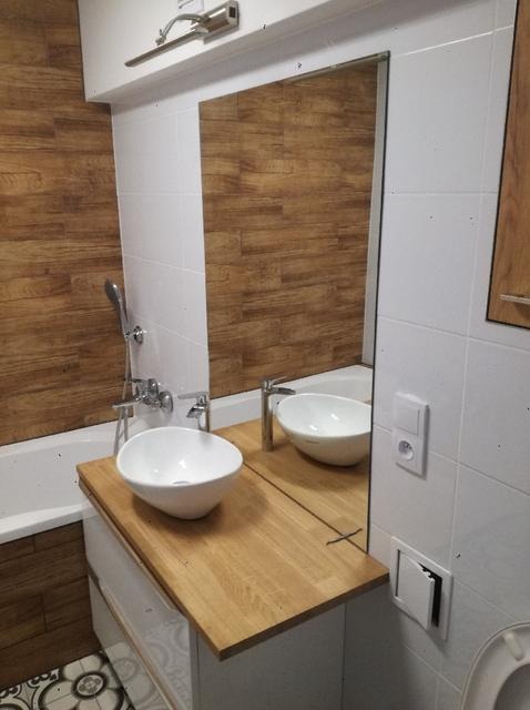 Umywalka nablatowa w łazience z drewnianą okładziną i białymi płytkami, widoczne detale wykończenia i armatura.