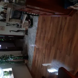 Ukończona podłoga z paneli drewnopodobnych w salonie z kominkiem, widoczne przejście między panelami a kamienną posadzką kominka, oraz drewniana żyrafa jako element dekoracyjny.