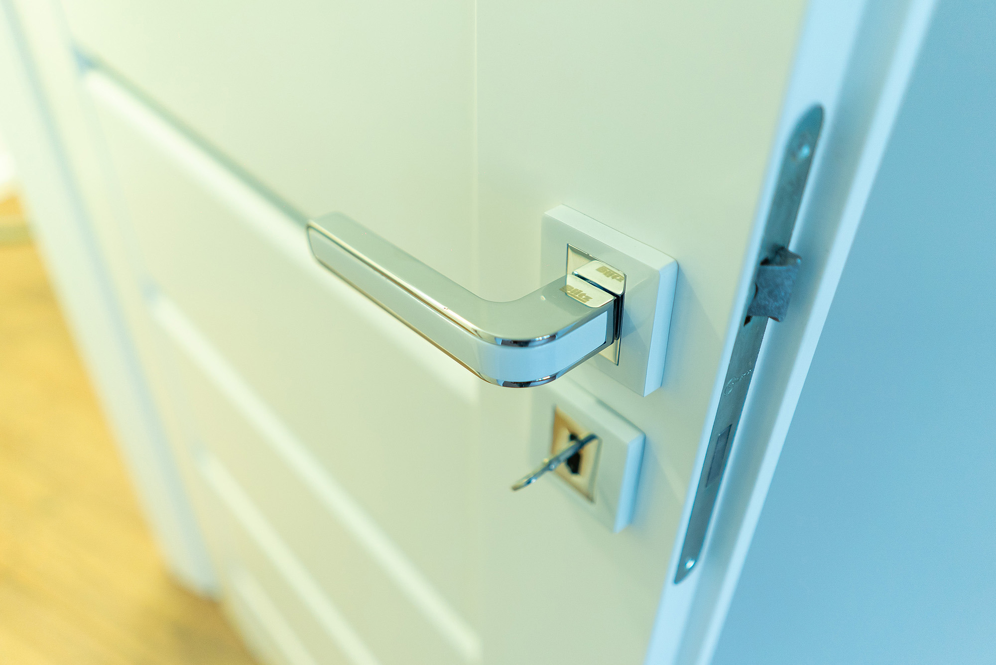 Białe drzwi z nowoczesną, chromowaną klamką i kluczem w zamku, zamontowane przez firmę z Ełku.