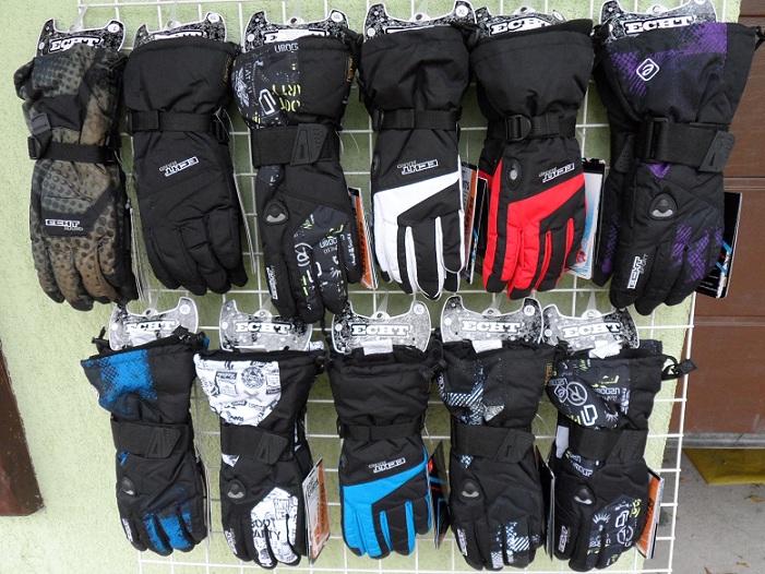 Rękawice narciarskie włoskiej marki Echt i YDI, różne wzory i kolory, wiszące na metalowym stojaku.