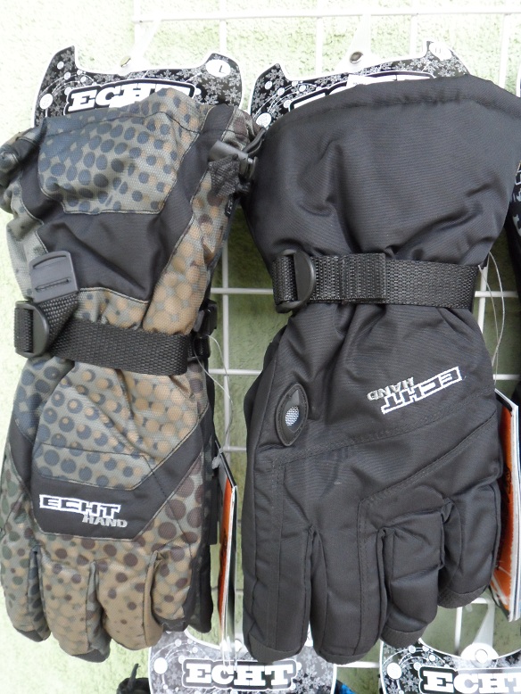 Dwie rękawice narciarskie marki Echt, jedna w kolorze czarnym, druga z wzorem w kropki, wiszące na metalowej siatce.