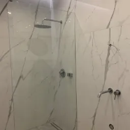 Kabina prysznicowa typu walk-in z armaturą w kolorze chromu i odpływem liniowym, wykończona płytkami imitującymi marmur Carrara.