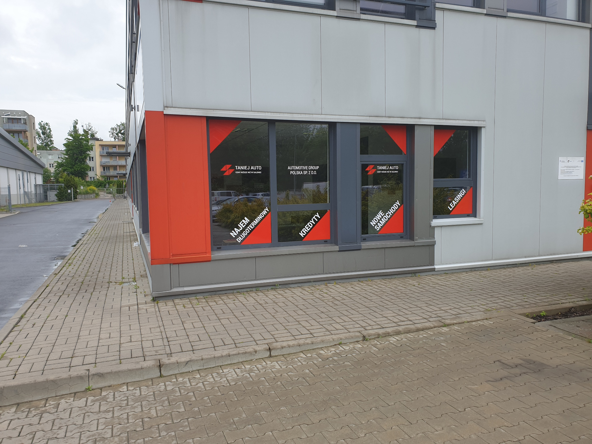 Budynek firmy Automotive Group Polska Sp. z o.o. w Łodzi z reklamami na oknach informującymi o najmie długoterminowym, kredytach, nowych samochodach i leasingu.