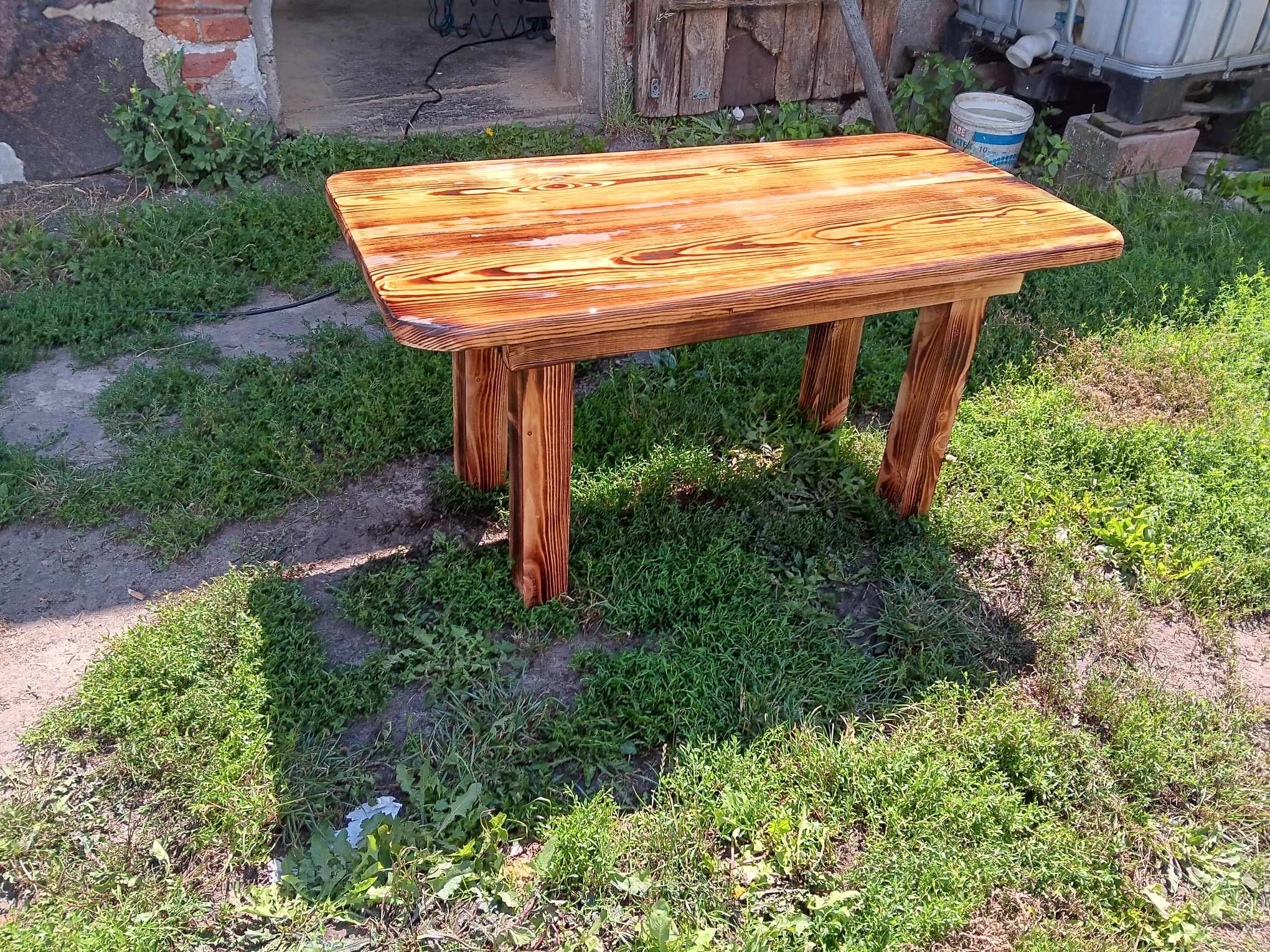 Drewniany stolik z polerowanym blatem, stojący na trawie przed budynkiem gospodarczym.