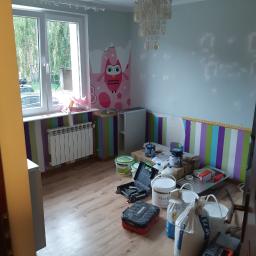 Stiver-Bud - Pokój w trakcie malowania, widoczne puszki z farbą, narzędzia malarskie, ściany częściowo pomalowane, na jednej ścianie tapeta z motywem sowy, okno z widokiem na zieleń.