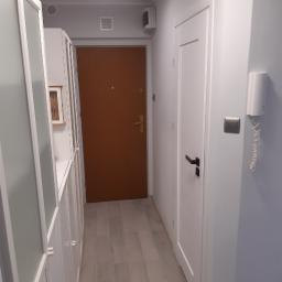 Stiver-Bud - Nowoczesny przedpokój z białymi meblami w zabudowie, drewnianymi panelami podłogowymi i brązowymi drzwiami wejściowymi, oświetlony okrągłą lampą sufitową z czarnym abażurem.