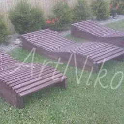 Trzy drewniane leżaki ogrodowe z listew, ustawione na trawniku przed żywopłotem z tujami. Na zdjęciu widoczne jest logo firmy ArtNiko.