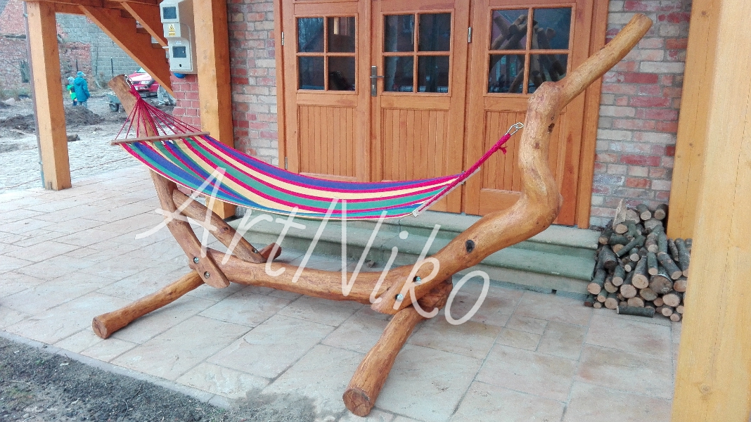 Ręcznie robiony hamak z drewna, zawieszony na werandzie z drewnianymi drzwiami i stosem drewna opałowego w tle.