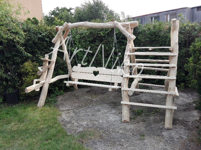 Drewniana huśtawka ogrodowa z drabinką, wykonana z surowego drewna, z wyciętym sercem na oparciu, zawieszona na łańcuchach, otoczona zielenią.