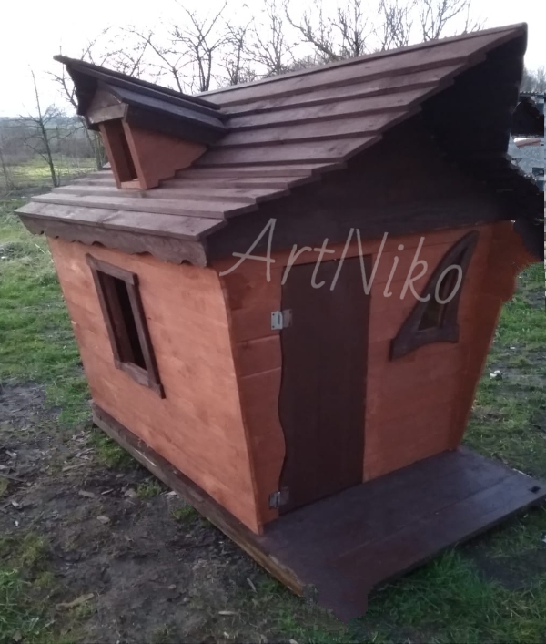 Nietypowa, drewniana, pomalowana na brązowo i pomarańczowo altana dziecięca z oknami o fantazyjnych kształtach, umieszczona na trawie.
