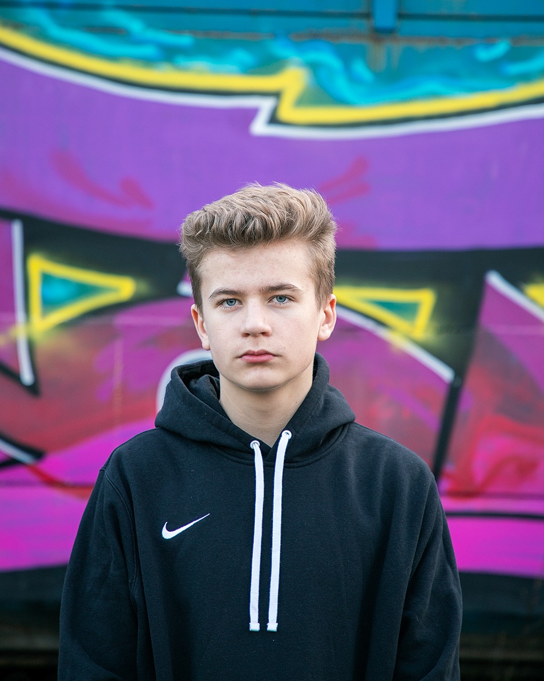 Portret młodego chłopca w czarnej bluzie z kapturem na tle kolorowego graffiti.