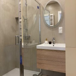 wolanskainteriors - Nowoczesna łazienka w beżowych odcieniach z przeszkloną kabiną prysznicową, umywalką z szafką z drewnianym dekorem, okrągłym lustrem z podświetleniem i minimalistyczną armaturą.