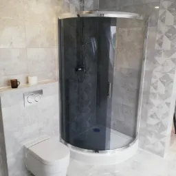 Nowoczesna łazienka z kabiną prysznicową typu walk-in z ciemnymi szybami, wiszącą toaletą i płytkami w odcieniach szarości z geometrycznymi wzorami.