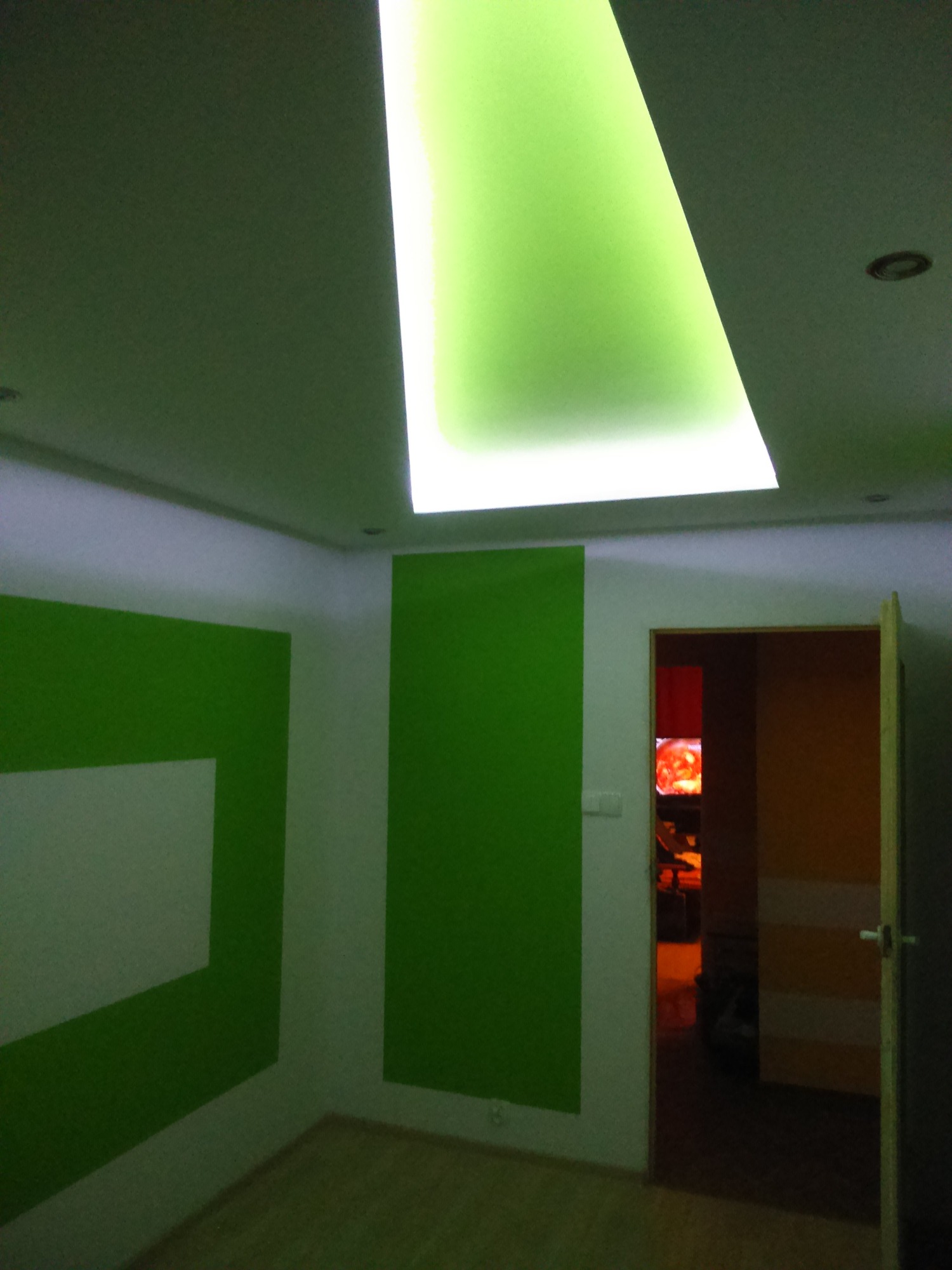 Wnętrze pokoju w Świeciu po malowaniu, z zielonymi akcentami na ścianach i podświetlanym sufitem, widok na otwarte drzwi do kolejnego pomieszczenia.