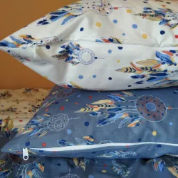 Stos poduszek z motywem łapaczy snów, biała i szara, z widocznymi zamkami błyskawicznymi.