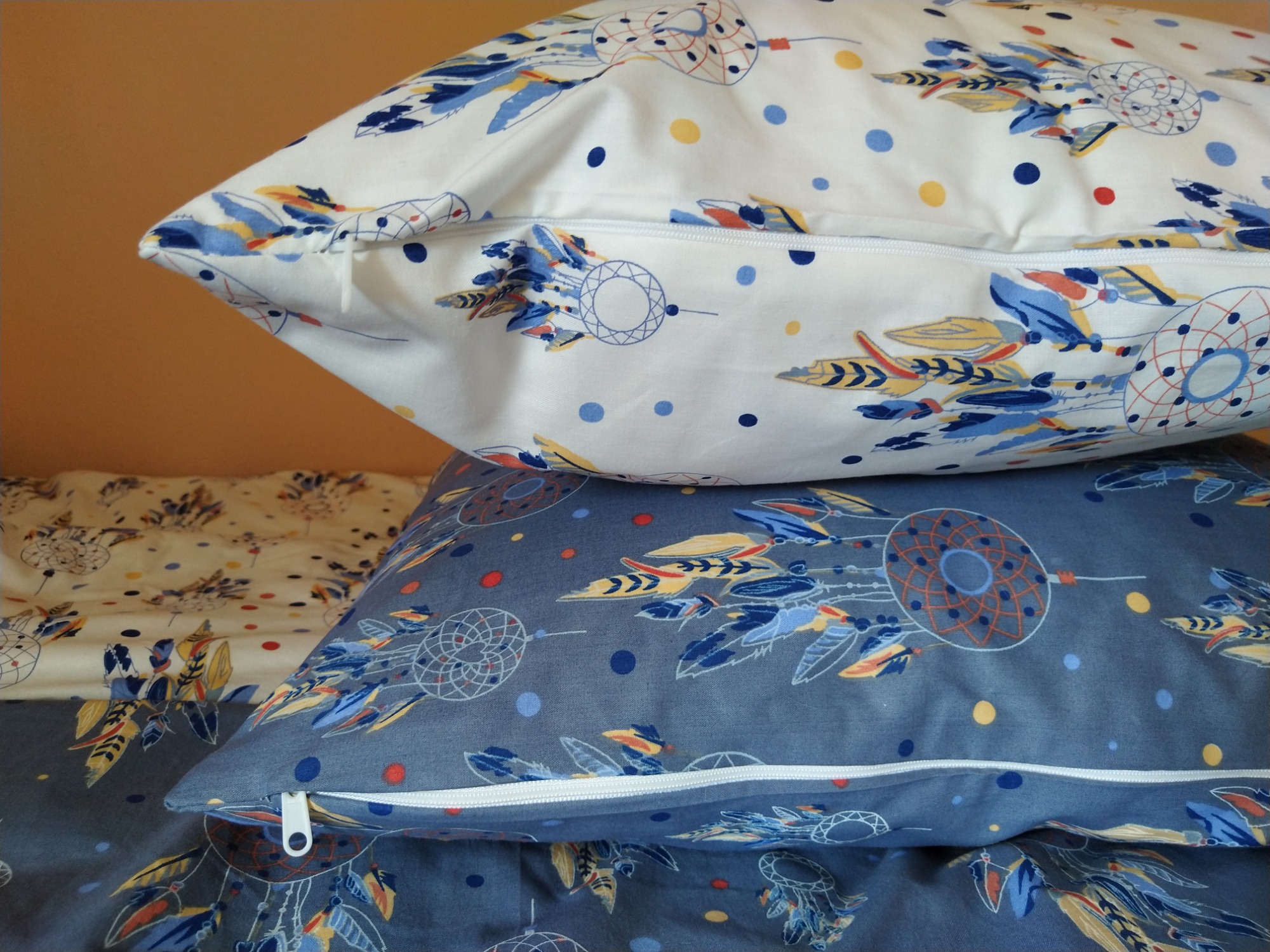 Stos poduszek z motywem łapaczy snów, biała i szara, z widocznymi zamkami błyskawicznymi.