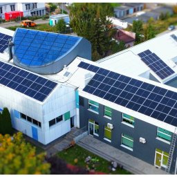 GooSun - Widok z góry na budynek z zainstalowanymi panelami słonecznymi na dachu, gdzie jeden pracownik montuje dodatkowy panel, drabina oparta o ścianę budynku.