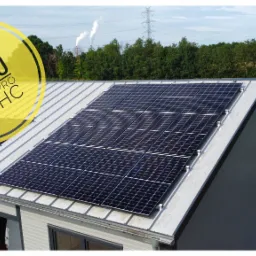 Panel słoneczny Jinko Tiger Pro 60 HC o mocy 5.4 kWp zamontowany na metalowym dachu budynku gospodarczego, w tle słupy wysokiego napięcia i komin