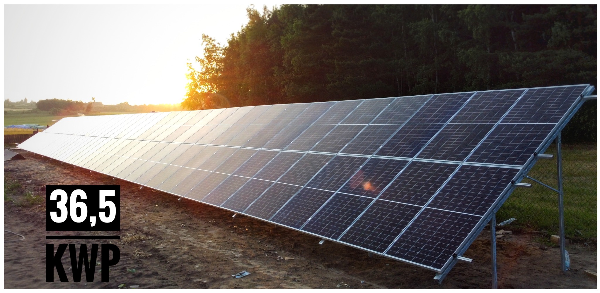 Długa instalacja fotowoltaiczna 36,5 kWp na ziemi, z widocznym zachodzącym słońcem i lasem w tle.